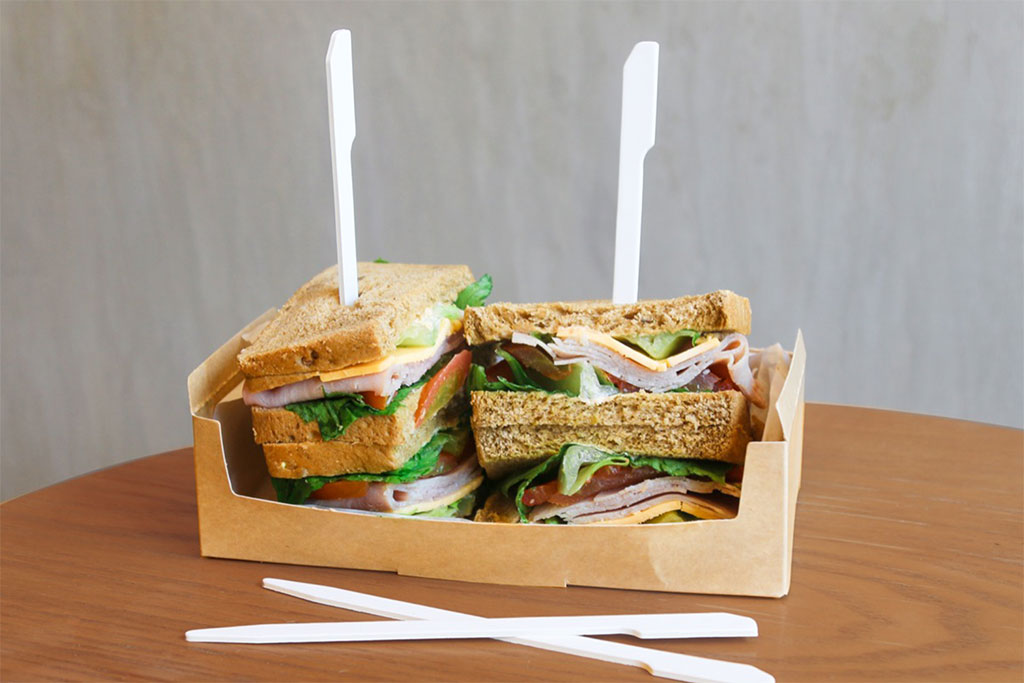 Sandwiches served in an eco-friendly cardboard container accompanied by white paper knives,